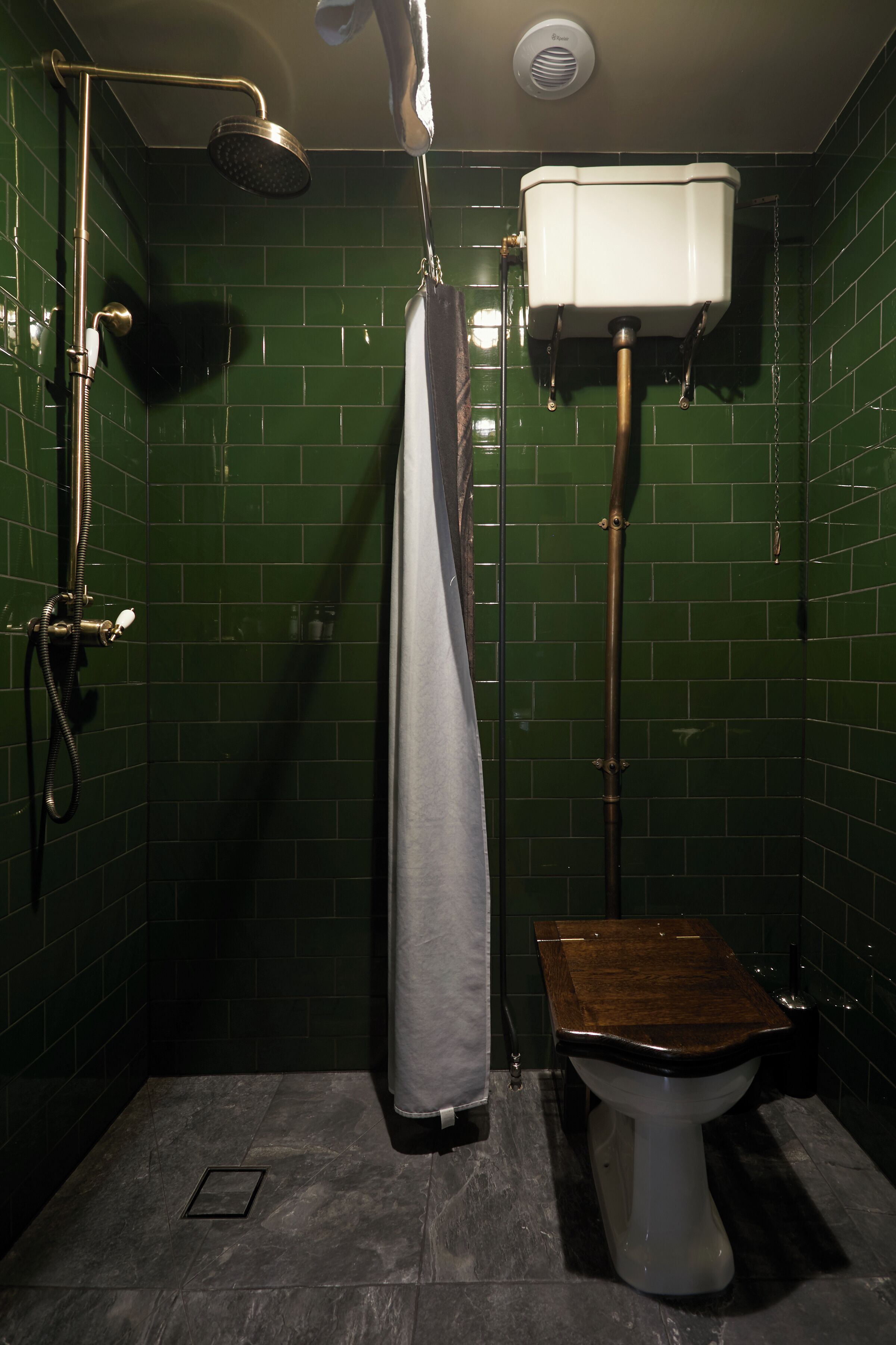 A bathroom with green tiled walls, a shower, a toilet, and a towel hanging on the wall.