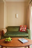 A green sofa with a red pillow, a wooden table with a bowl of green apples, and a book.
