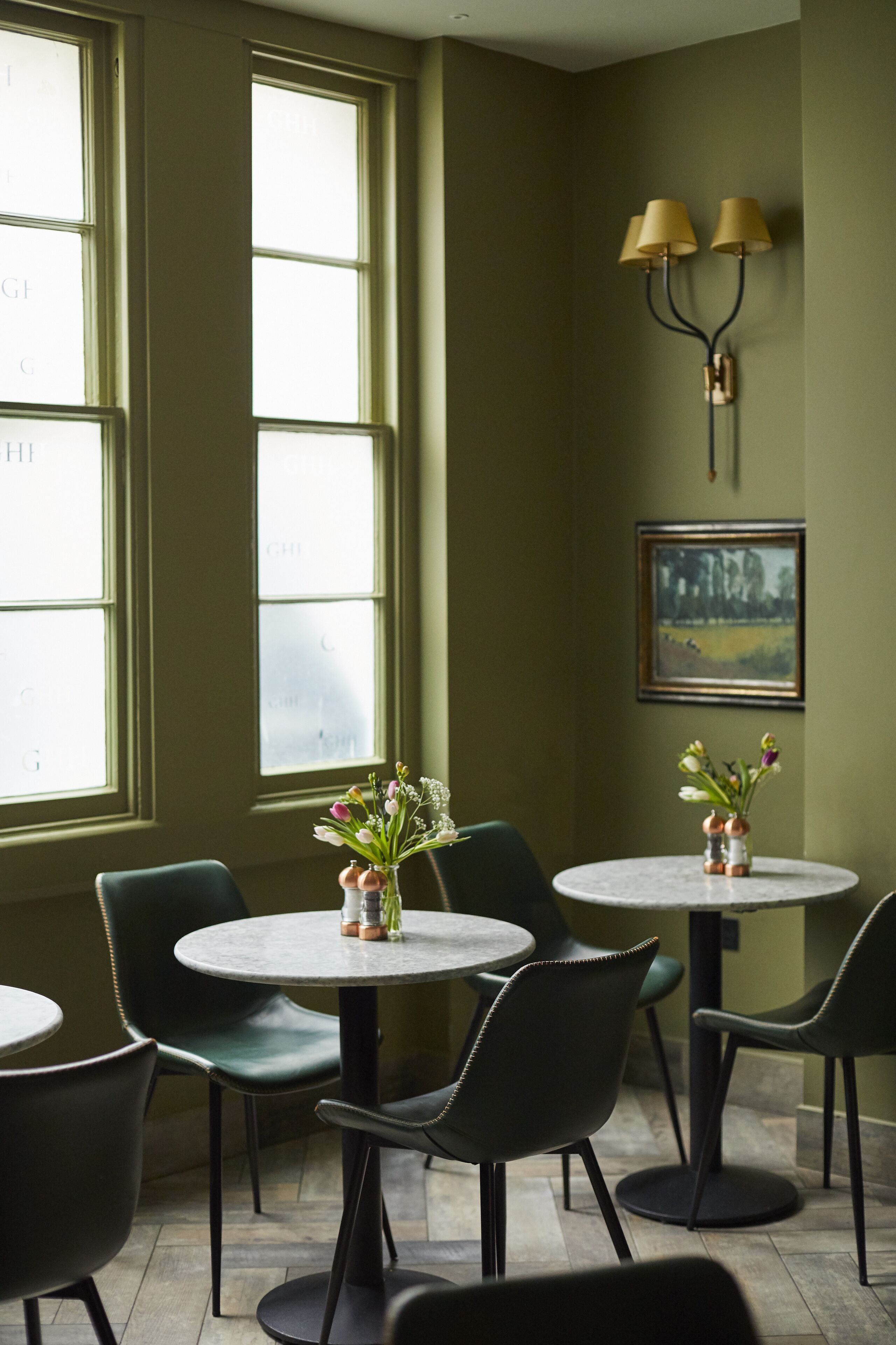 A dining area with round tables and chairs, a vase with flowers, and a painting on the wall.