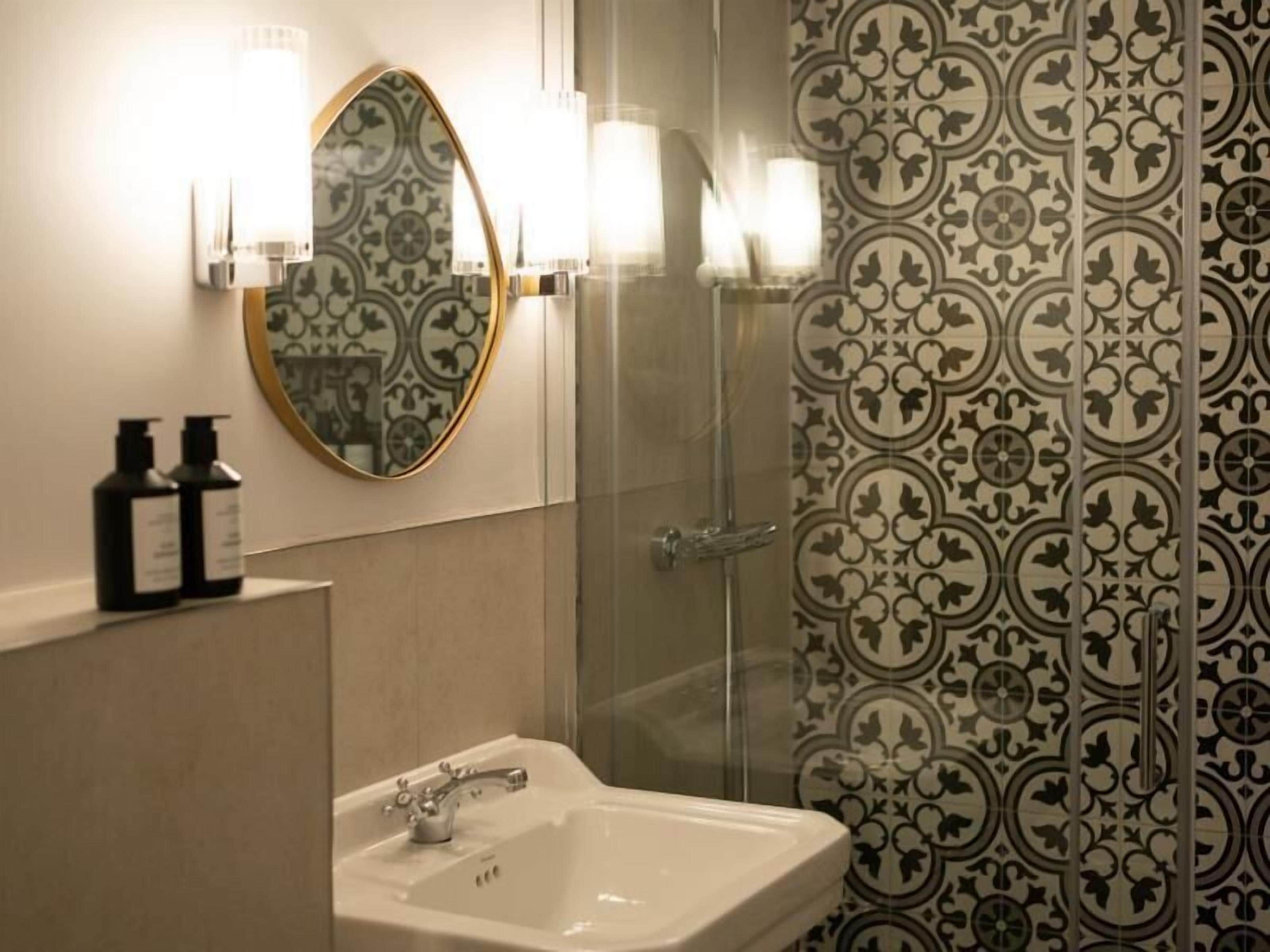 A bathroom with a white sink, a mirror with a gold frame, and patterned wallpaper.