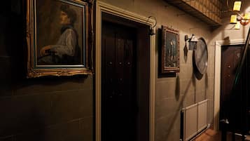 A dimly lit hallway with wooden flooring, a staircase, and framed artwork on the walls.