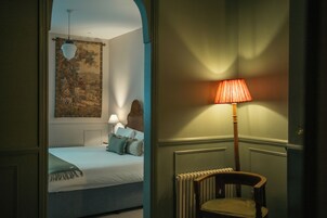 Ein Schlafzimmer mit einem Bett, einem Sessel, einer Lampe und Wandteppich.