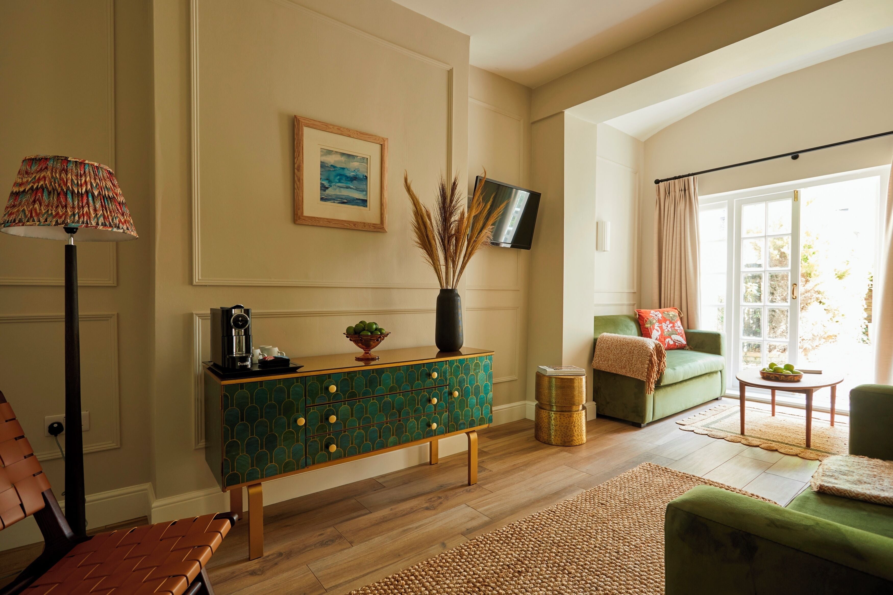 Un salon comprenant une console à motifs verts, un lampadaire, un canapé vert et un téléviseur fixé au mur.