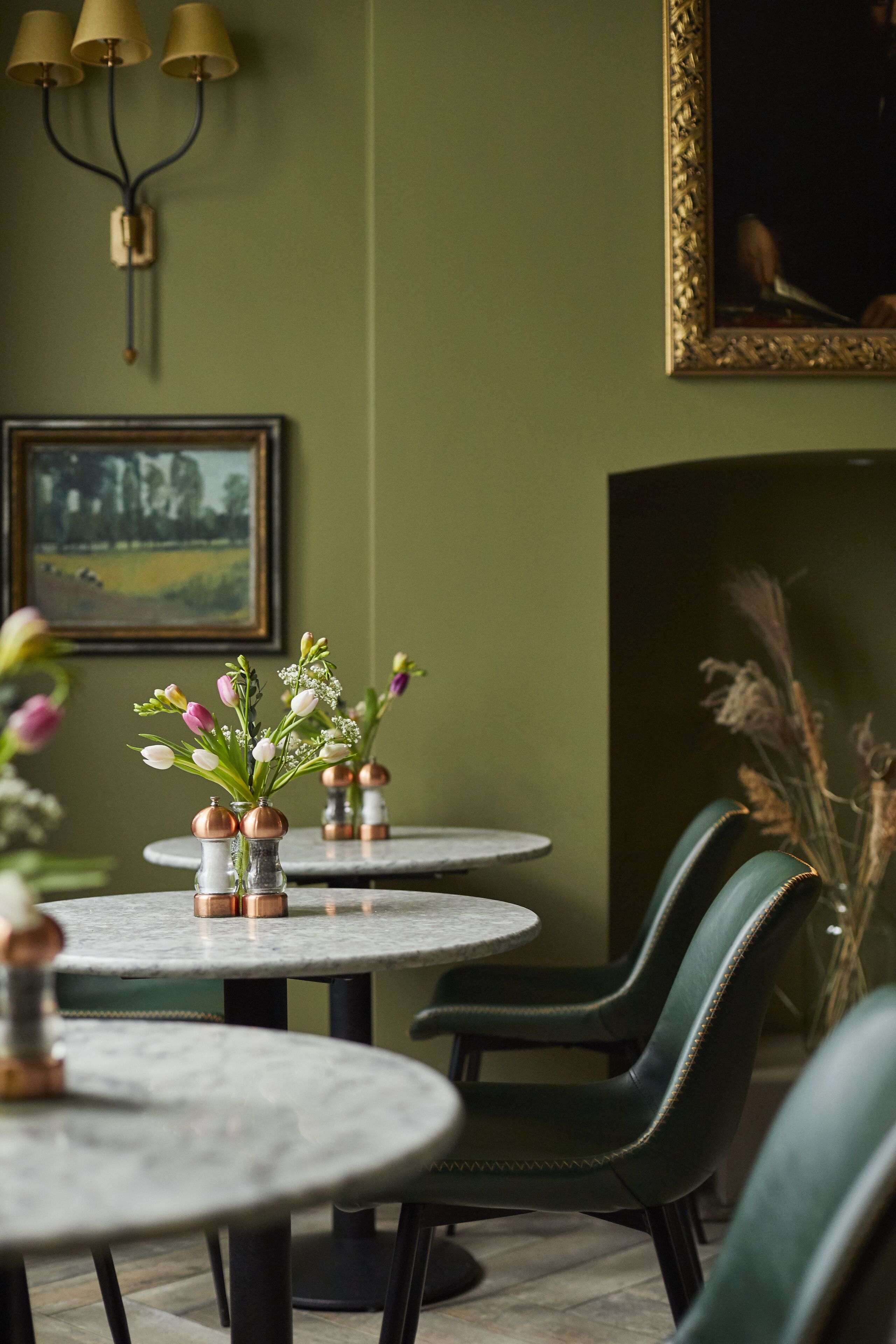 Un comedor con mesas redondas, sillas verdes y jarrones con flores.