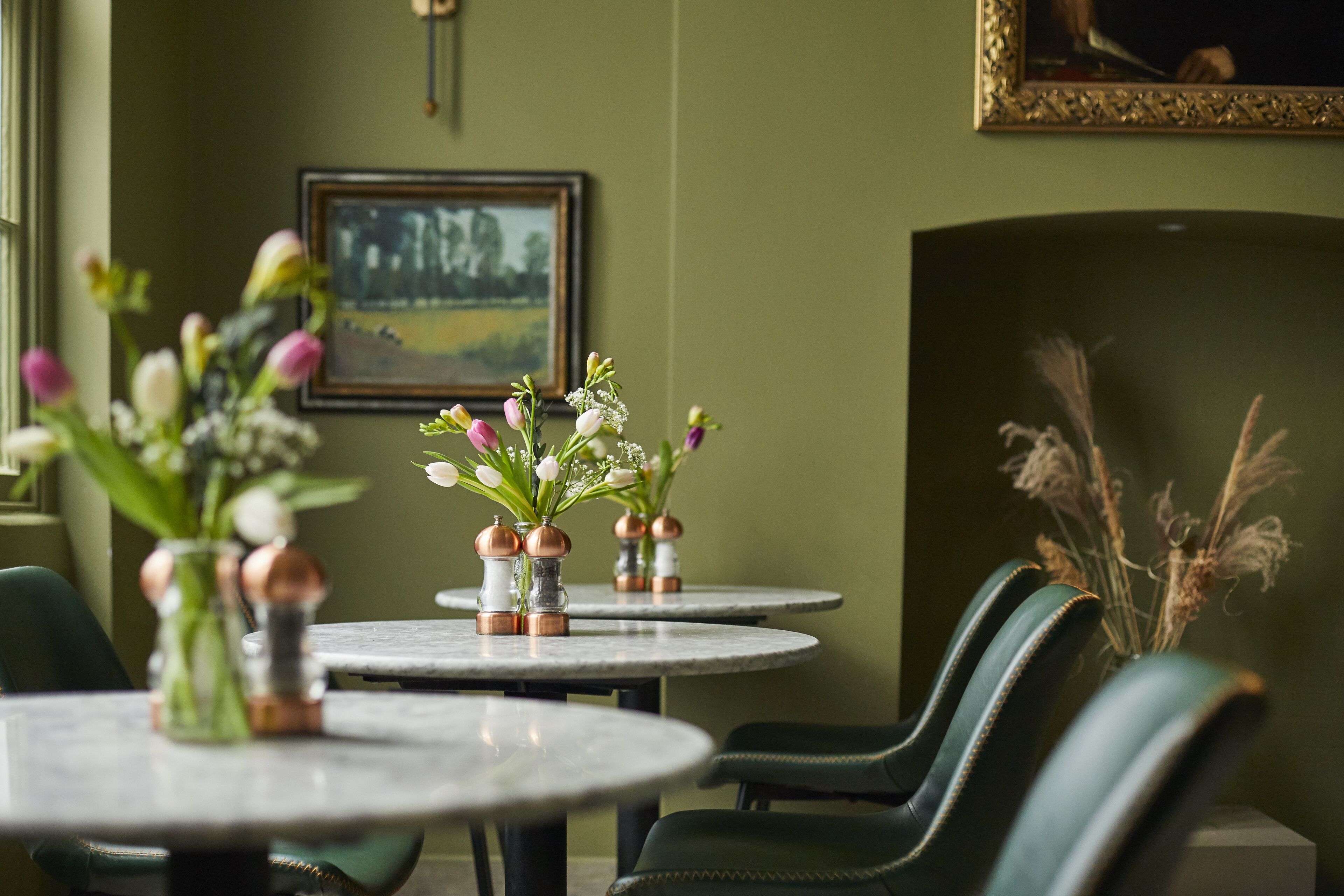 A dining area with round tables, green upholstered chairs, and floral centerpieces.