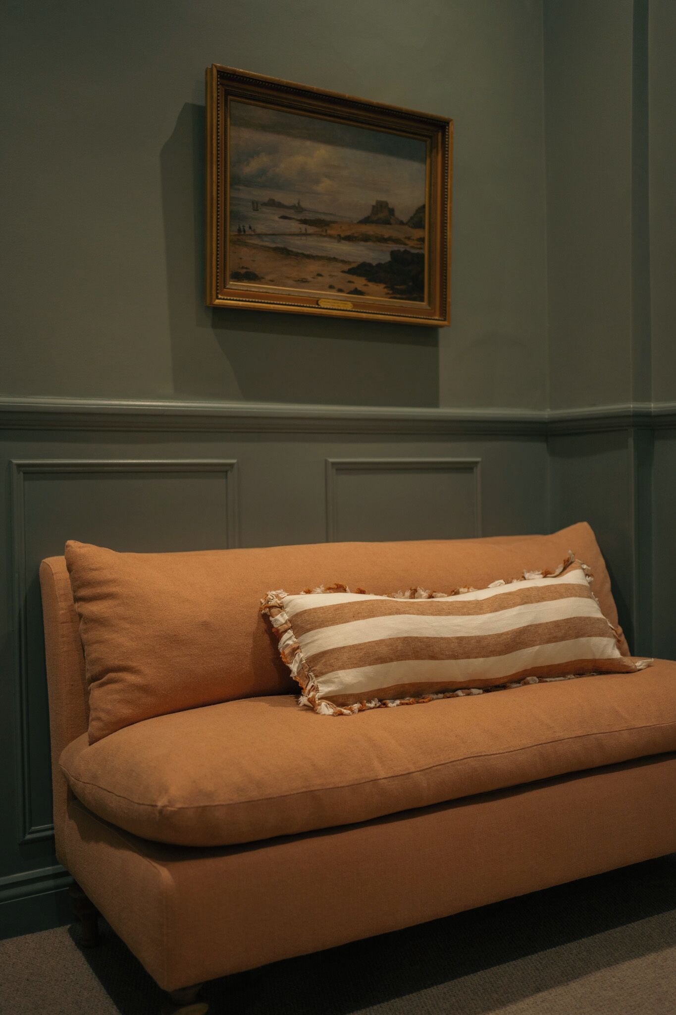 Una habitación con un sofá, un cuadro enmarcado en la pared y una puerta con paneles.