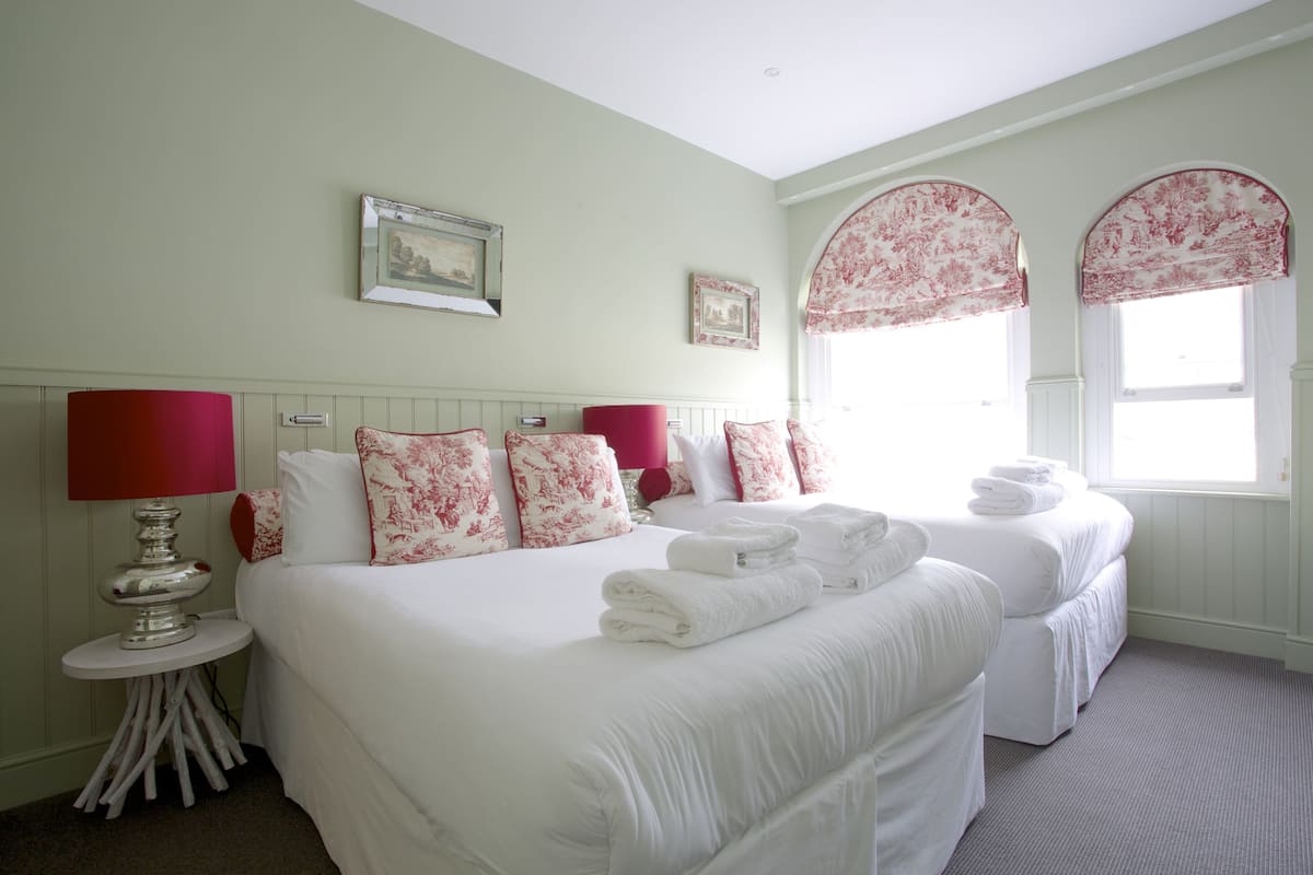 A hotel room with a large bed, two bedside tables, a red lamp, and floral-patterned curtains.