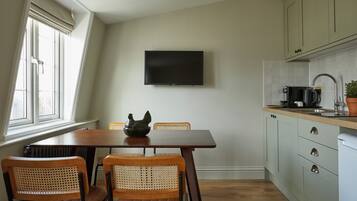 Een keuken met een eettafel, stoelen, een flatscreen televisie, kasten en een raam.
