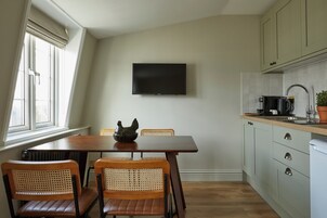 A kitchen with a dining table, chairs, a flat-screen TV, cabinets, and a window.