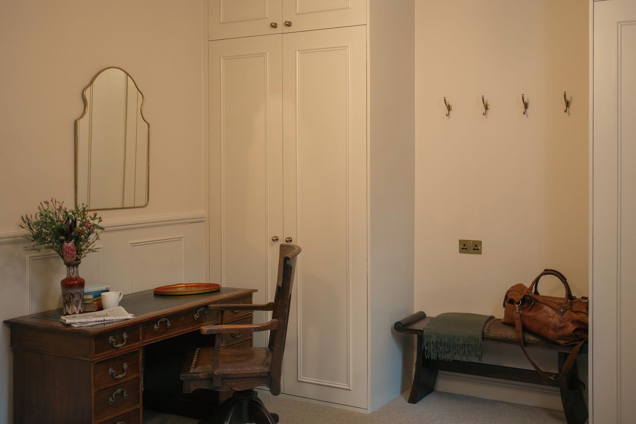 Une pièce comprenant un bureau, une chaise, une armoire et un banc sur lequel est posé un sac à main.