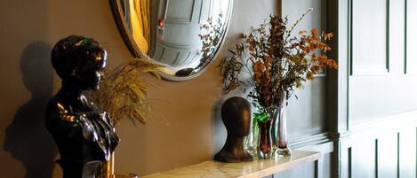 A reception area with a marble counter, a bust sculpture, a mirror, and a vase with dried flowers.