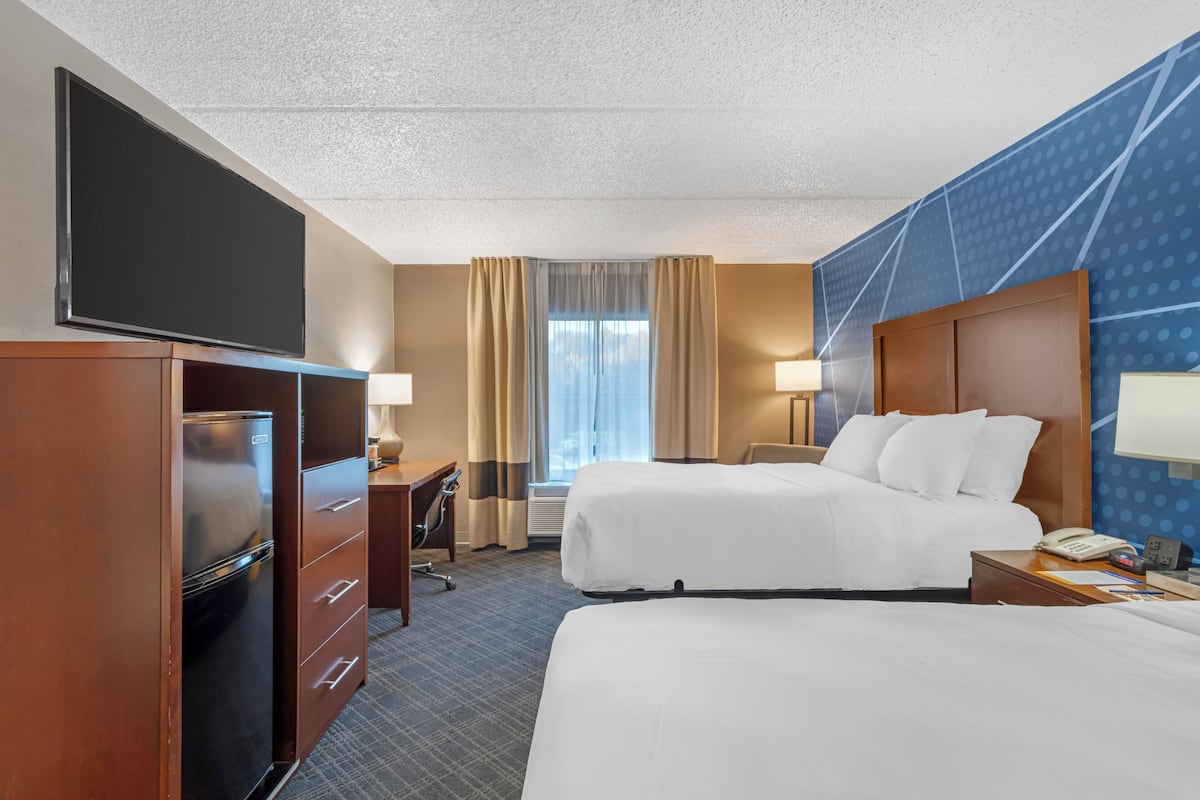 A hotel room with two beds, a TV, a desk, and a window with curtains.