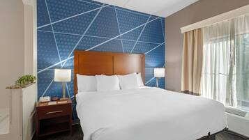 Een hotelkamer met een groot bed, twee nachtkastjes, een wand met een geometrisch patroon en een raam met gordijnen.