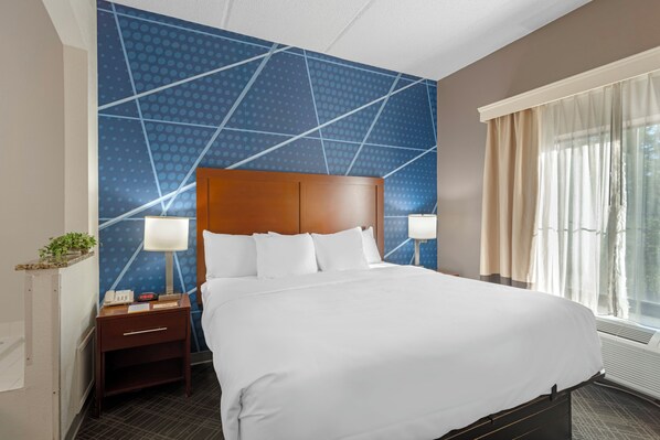 A hotel room with a large bed, two bedside tables, a nightstand, a wall with a geometric pattern, and a window with curtains. - Comfort Inn & Suites Spartanburg North (Spartanburg)