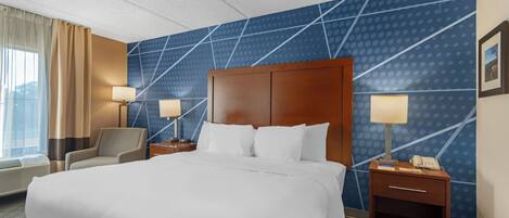 A hotel room with a large bed, two bedside tables with lamps, a chair, and a wall with a geometric pattern.