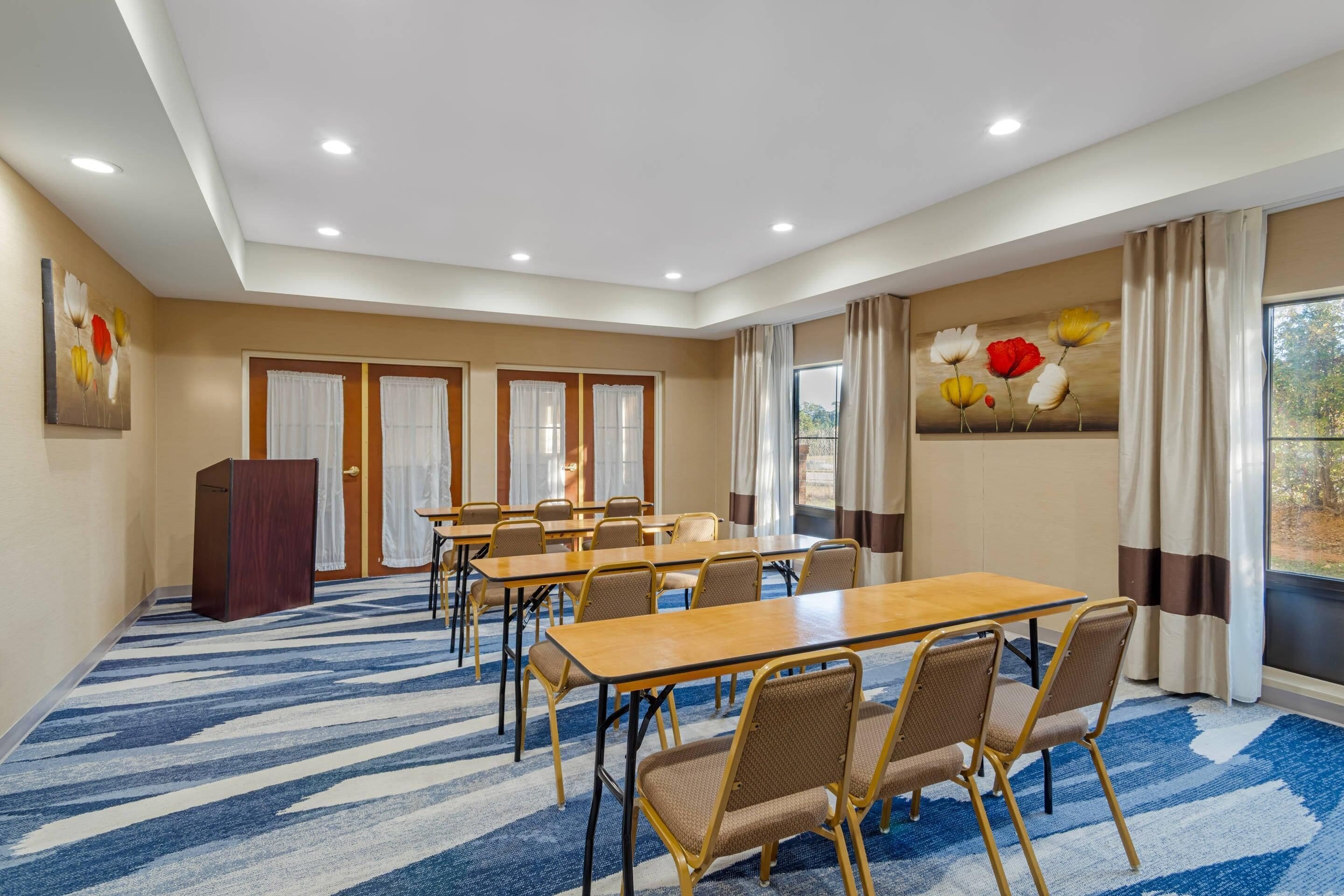 A conference room with a blue patterned carpet, beige walls, and a large window with curtains.