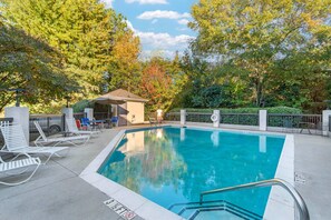 A swimming pool with lounge chairs and a covered seating area, surrounded by trees and a fence. - Comfort Inn & Suites Spartanburg North (Spartanburg)
