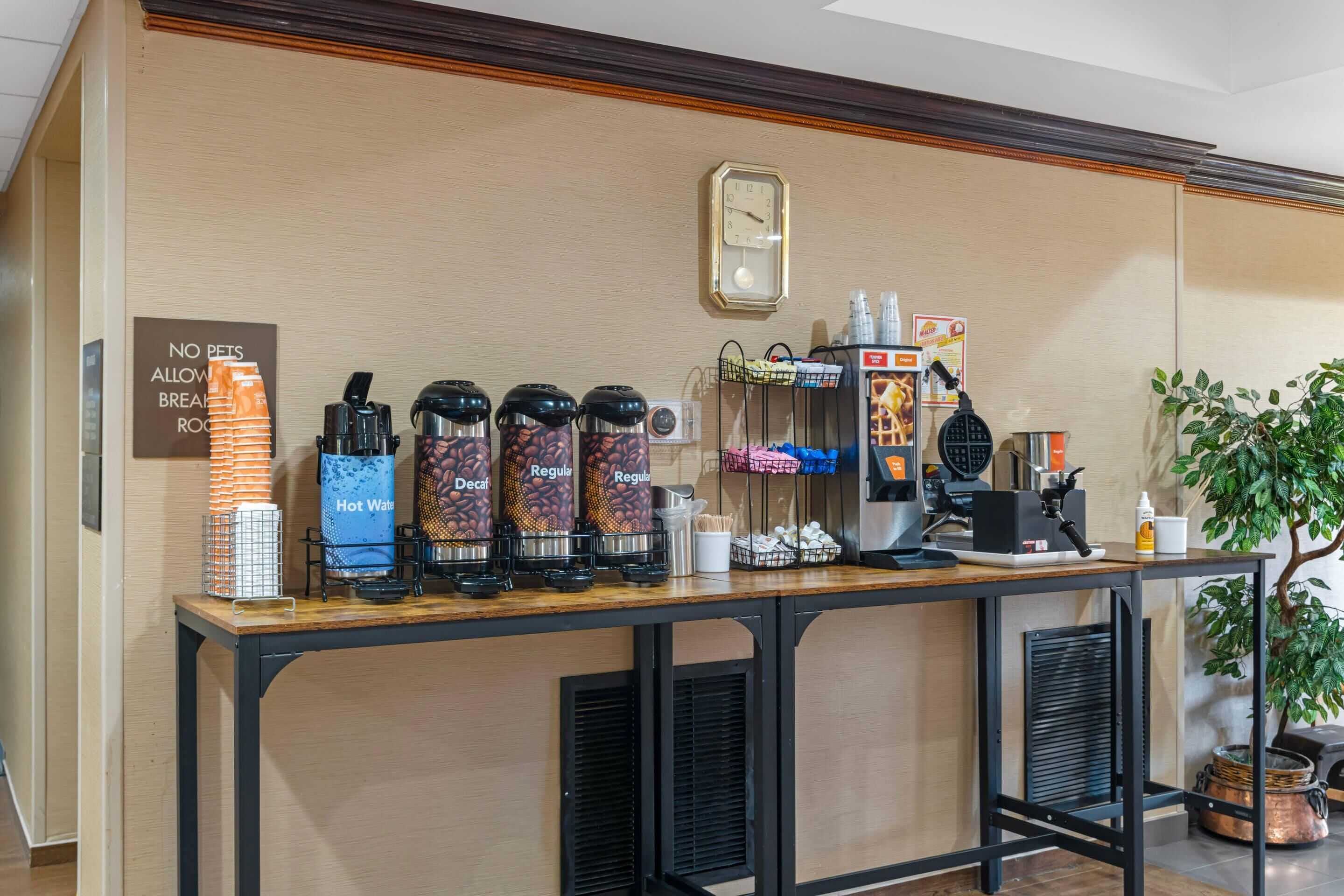 Een koffiehoek met meerdere koffiezetapparaten, een klok en een bord waarop huisdieren verboden zijn.