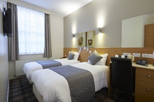 A hotel room with two beds, a desk, a chair, a TV, and artwork on the wall.