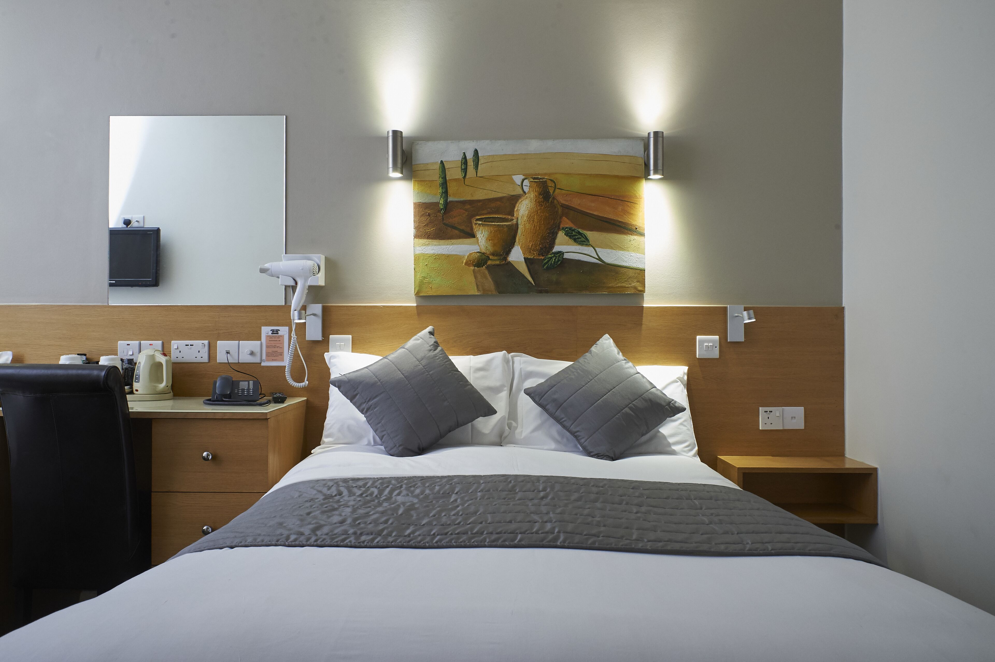 Ein Hotelzimmer mit Bett, Nachttisch, Lampe und einem Bild an der Wand.
