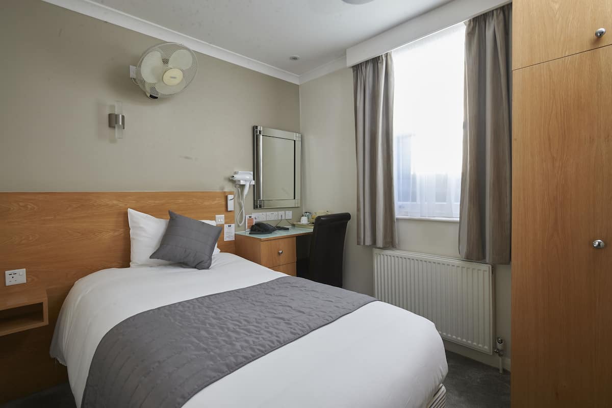 A hotel room with a bed, bedside table, mirror, and a window with curtains.