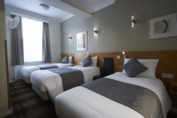 A hotel room with three beds, a large window with curtains, wall-mounted lights, and a framed picture. - Luna Simone Hotel (London)