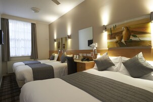 Quarto de hotel com duas camas, uma escrivaninha, telefone e um quadro na parede.