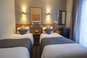 Ein Hotelzimmer mit zwei Betten, einem Nachttisch, einem Spiegel und einem Bild an der Wand.