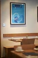 Ein gerahmtes abstraktes Kunstwerk an einer Wand, ein hölzernes Kopfteil und ein Tisch mit Tasse und Untertasse.