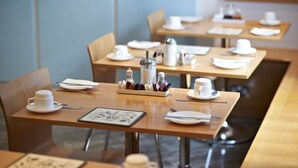 Un comedor moderno y limpio con mesas de madera dispuestas para el desayuno, incluyendo tazas, platos y cubiertos.
