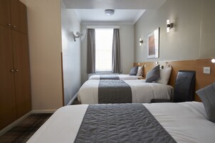 Ein Hotelzimmer mit zwei Betten, einem Schrank, einem Fenster mit Vorhängen und einer Wandleuchte.