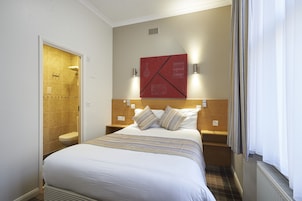 Ein Hotelzimmer mit Bett, Dusche, einem roten abstrakten Kunstwerk an der Wand und einem Fenster mit Vorhängen.