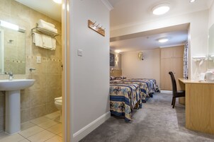 A bathroom with a sink, toilet, and towel rack. There are three beds with blue and beige bedding.