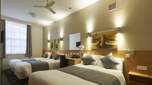 Habitación de hotel con dos camas, un escritorio, una silla, un ventilador de techo y obras de arte en las paredes.