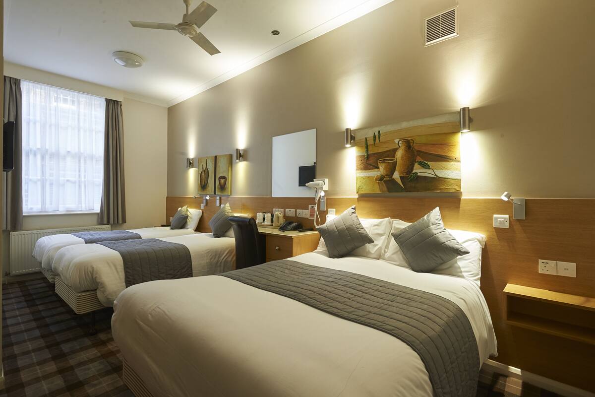 A hotel room with two beds, a desk, a chair, a ceiling fan, and artwork on the walls.