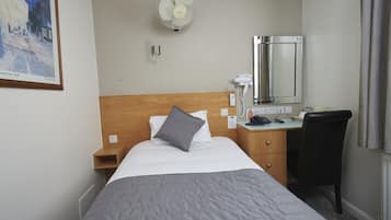 Une chambre d’hôtel avec un lit, un bureau, une chaise, un miroir, un ventilateur et un tableau au mur.