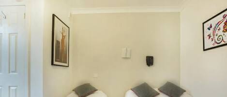 A hotel room with two single beds, a door, a framed picture on the wall, and a decorative wall piece.