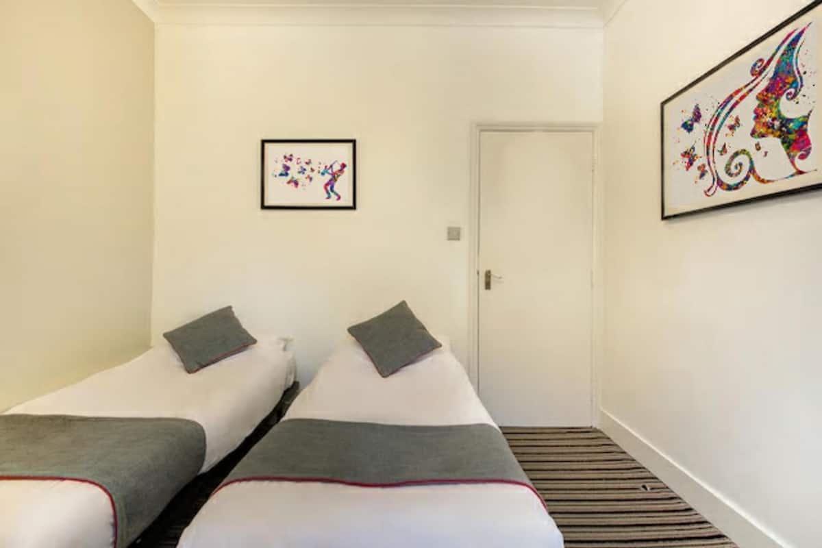 Habitación de hotel con dos camas individuales, una puerta y dos cuadros enmarcados en las paredes.