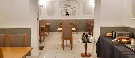 A dining area with multiple tables and chairs, a chandelier, and a buffet table with food items.