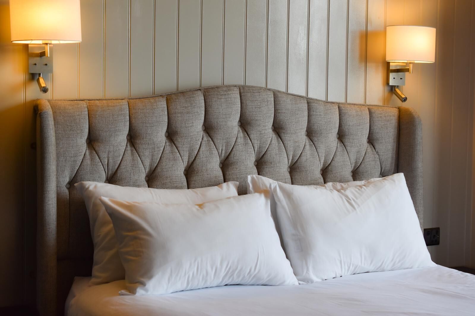 A bed with a tufted headboard, two wall-mounted lamps, and a wooden panel wall.