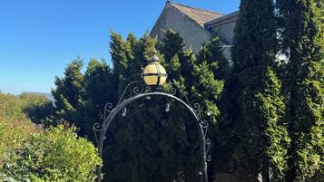 A street lamp with a spherical top and multiple light bulbs, surrounded by greenery and a building with a sloped roof.