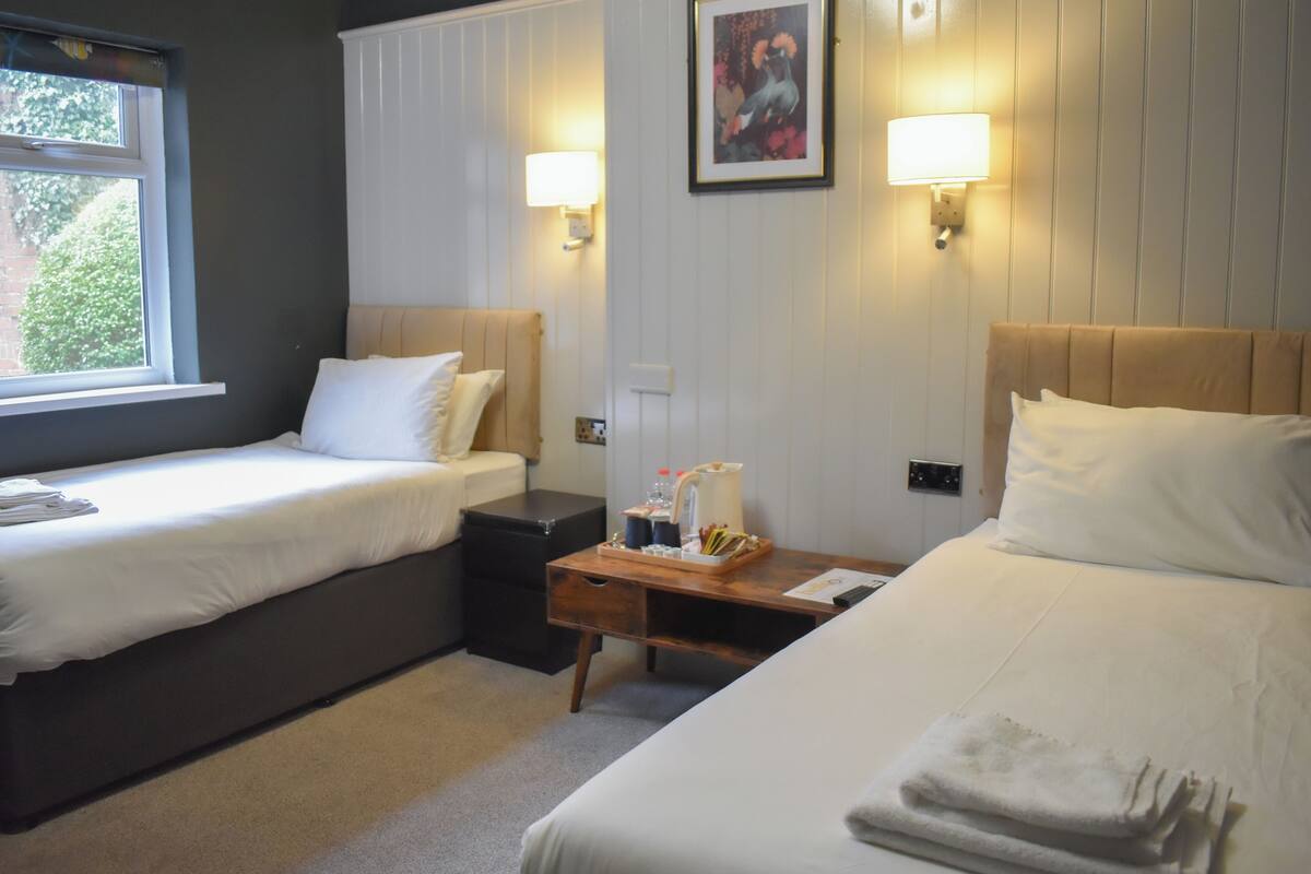 Habitación de hotel con dos camas, una mesita de noche, un escritorio, una ventana y lámparas fijadas a la pared.