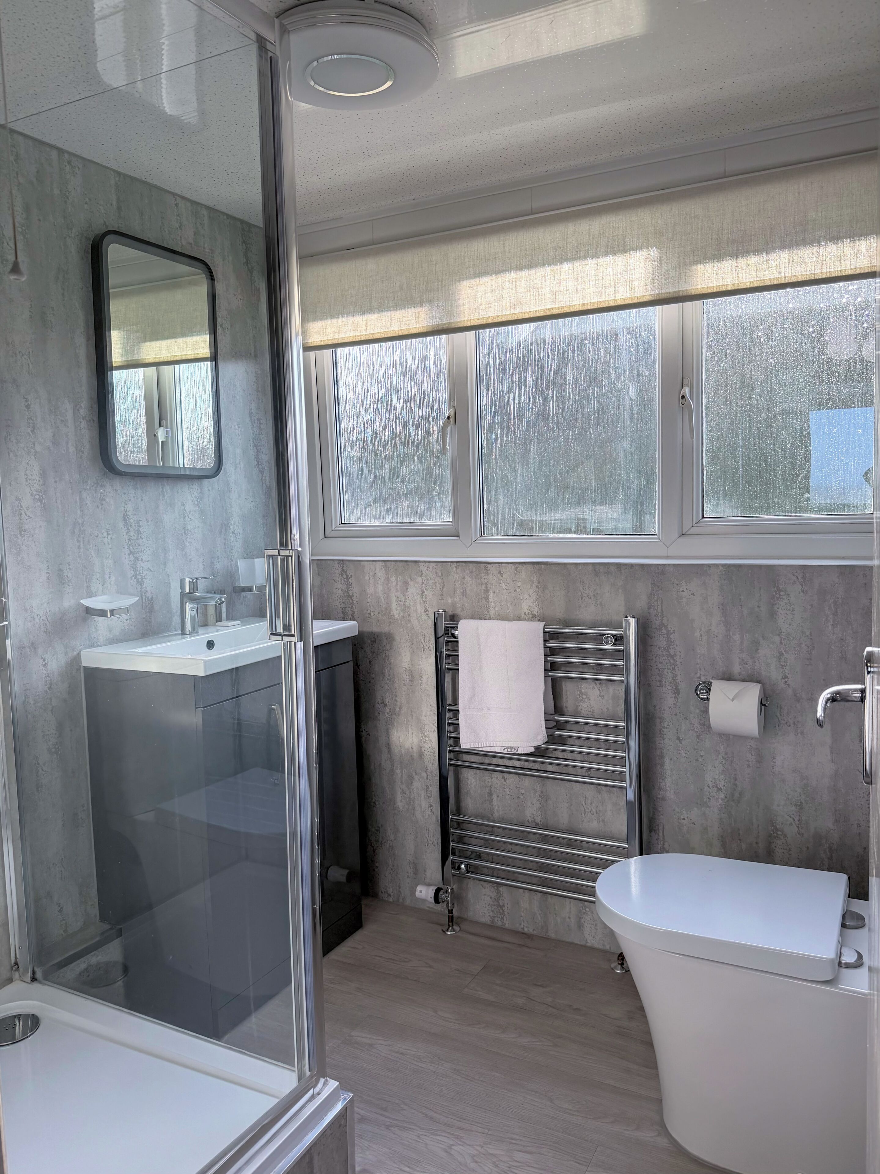 Et moderne badeværelse med en brusekabine i glas, en hvid vask, et toilet og en håndklædestang.
