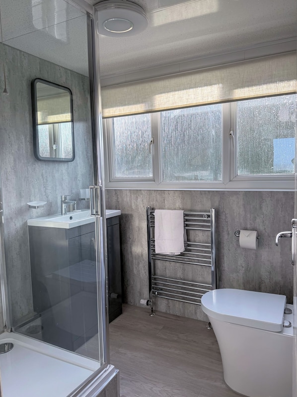 Un baño moderno con cabina de ducha de vidrio, un lavabo blanco, inodoro y barra para toallas.