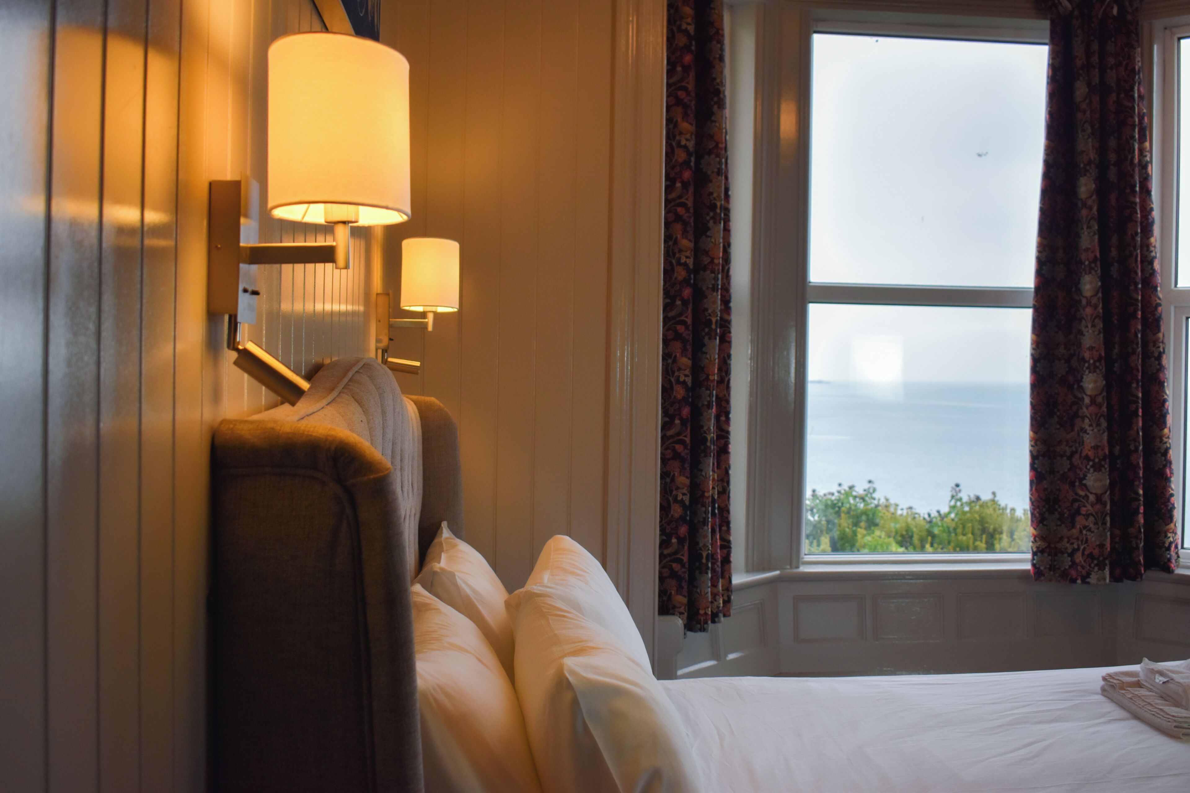 Habitación de hotel con una cama, dos lámparas de pared, una ventana con cortinas y vistas al exterior.