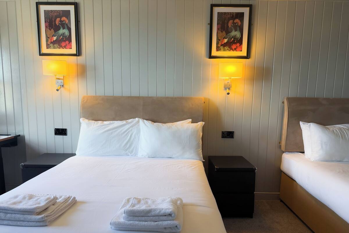 Habitación de hotel con una cama grande, dos mesitas de noche, un aparador y dos lámparas de pared.