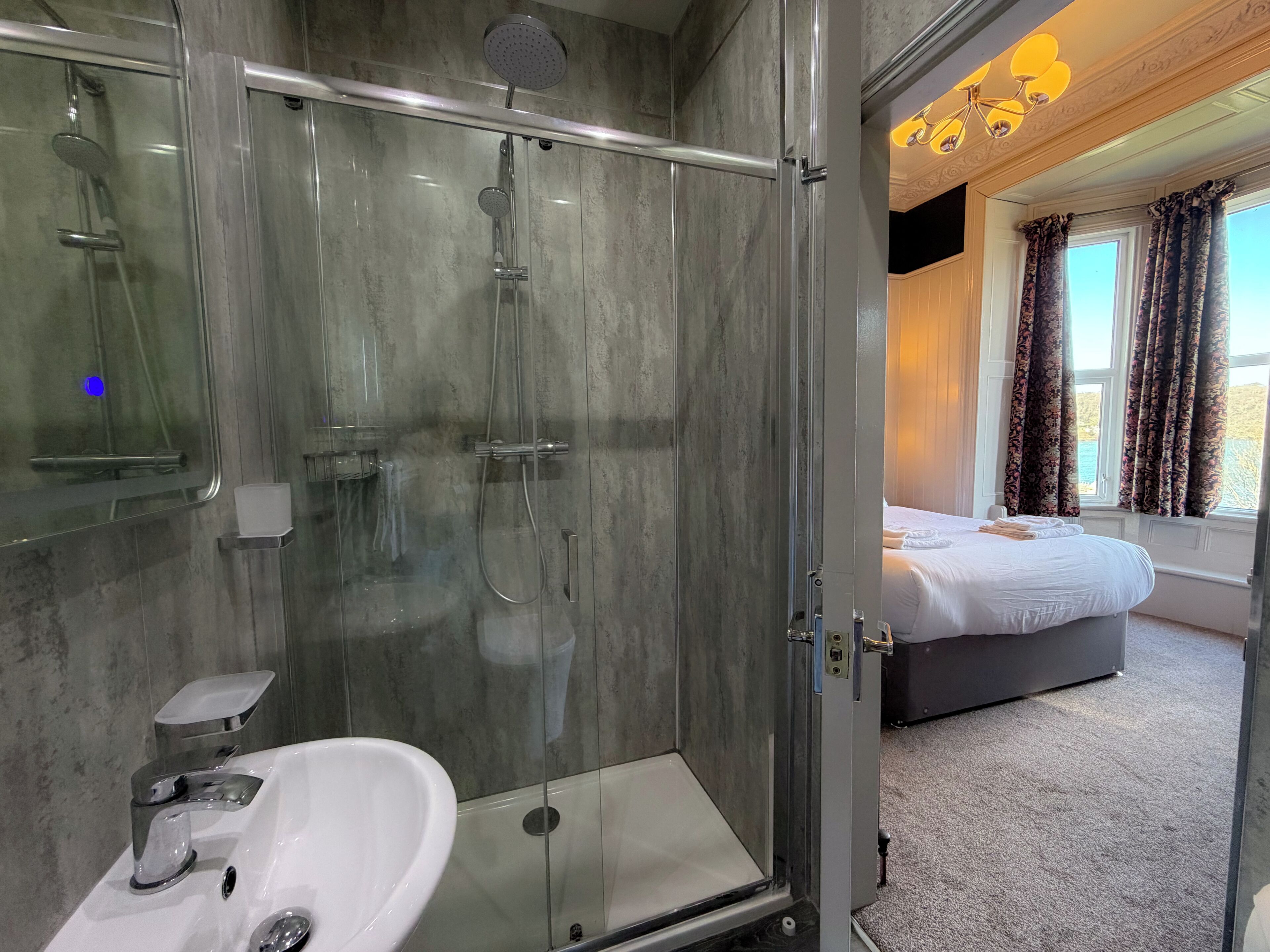 Un baño moderno con ducha envuelta en vidrio, lavamanos blanco y cabezal de ducha visible.