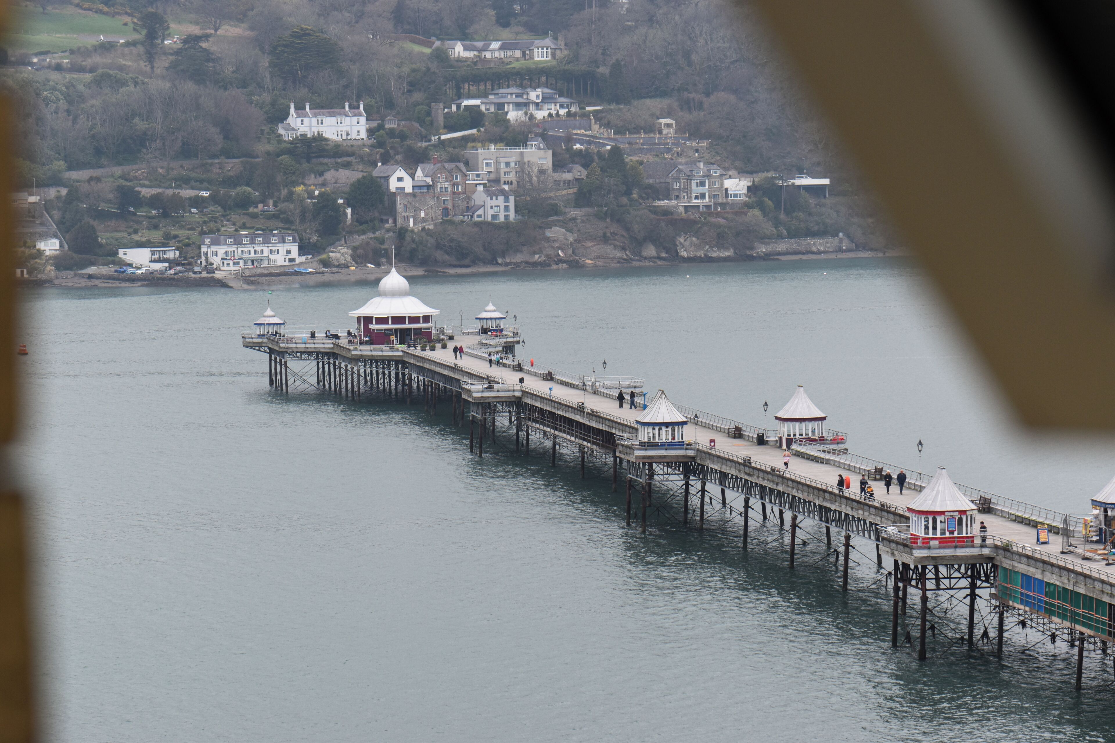 A pier extending into calm water with a row of small, white-roofed structures along its length.
