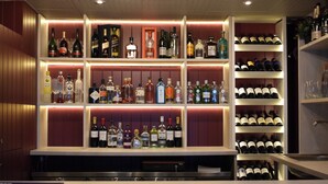 Zona de bar con estantes llenos de botellas de licor y vasos.