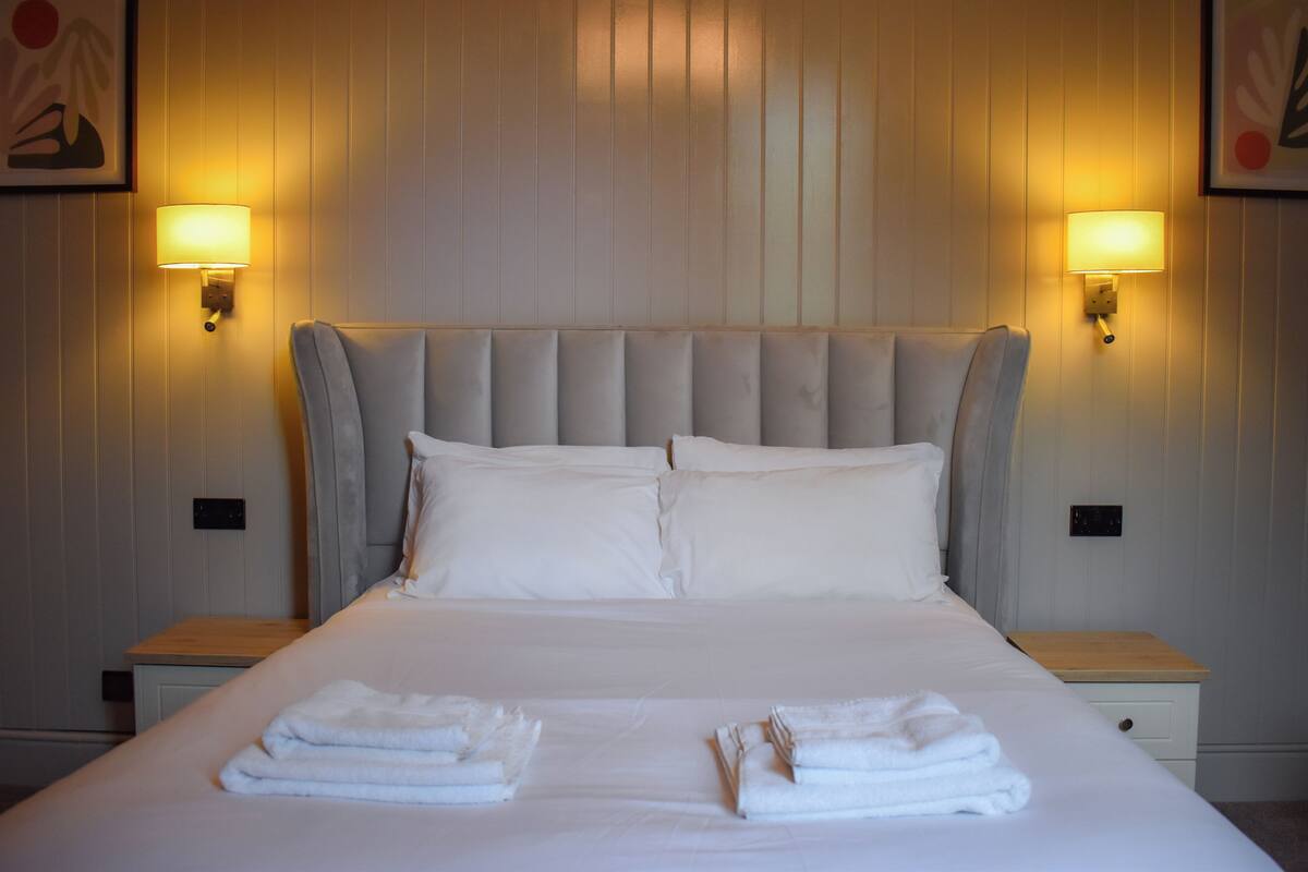 Habitación de hotel con una cama grande, dos mesitas de noche y lámparas fijadas a la pared.